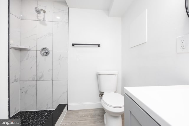 bathroom with a tile shower, vanity, hardwood / wood-style flooring, and toilet