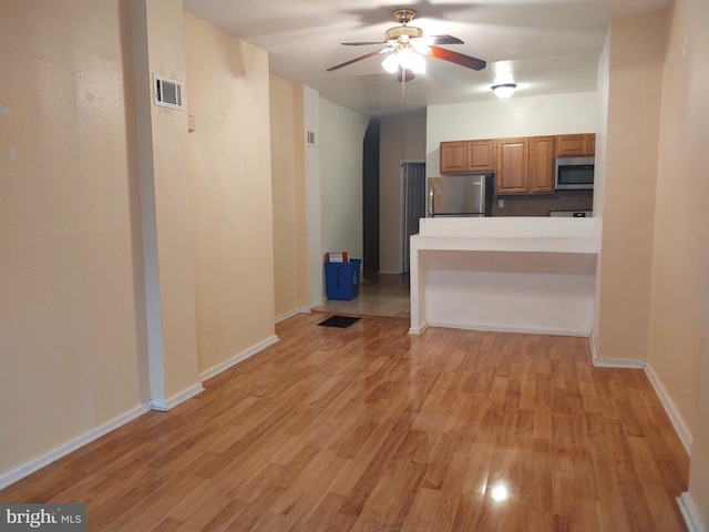 kitchen featuring ceiling fan, stainless steel appliances, a kitchen breakfast bar, light hardwood / wood-style floors, and kitchen peninsula