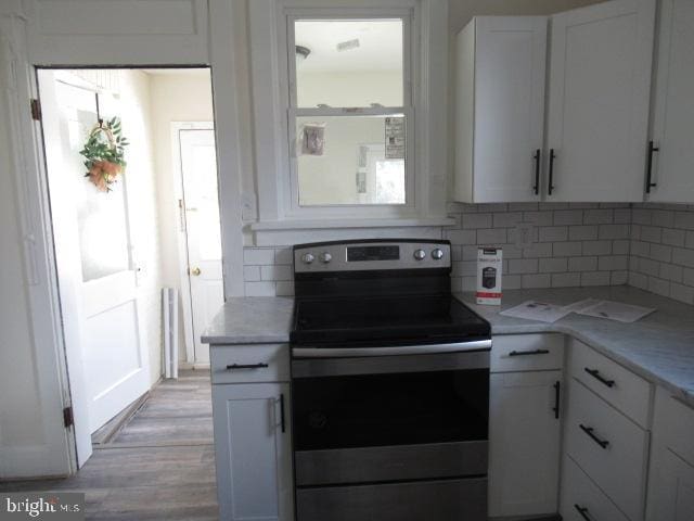 kitchen with electric stove, white cabinetry, light stone countertops, and decorative backsplash