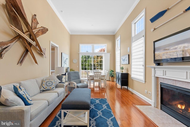 living room featuring a tile fireplace, ornamental molding, and light hardwood / wood-style floors