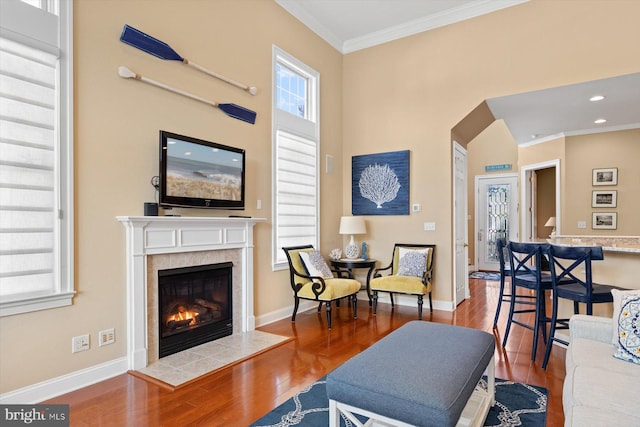 living room featuring wood-type flooring, ornamental molding, a tile fireplace, and a healthy amount of sunlight