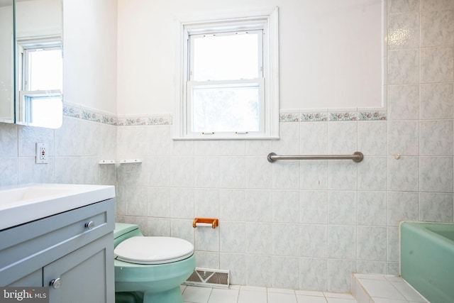 bathroom with tile walls, a bathtub, vanity, toilet, and tile patterned floors