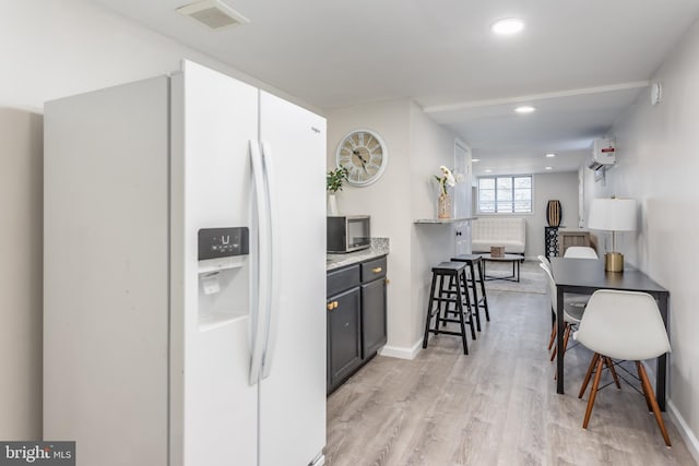 kitchen with light stone countertops, white refrigerator with ice dispenser, a wall unit AC, and light hardwood / wood-style floors