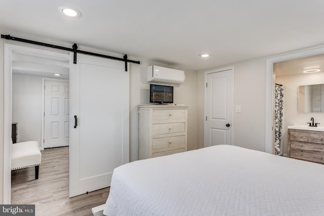 bedroom featuring sink, an AC wall unit, a barn door, and light wood-type flooring