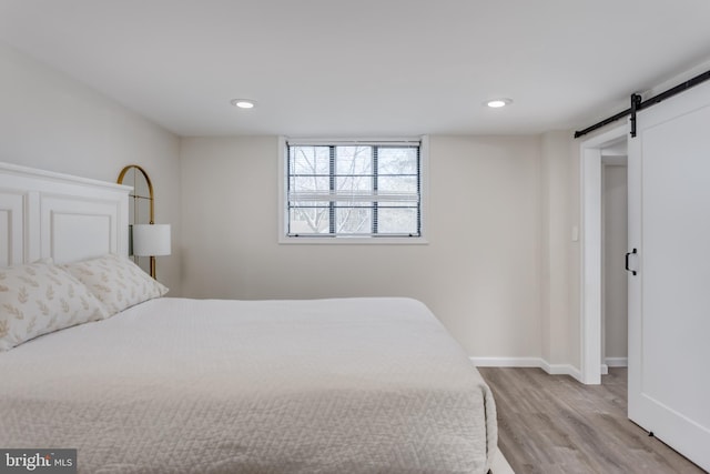 bedroom with a barn door and light wood-type flooring