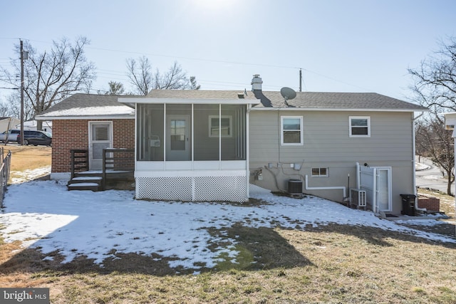 snow covered property with a sunroom and central AC