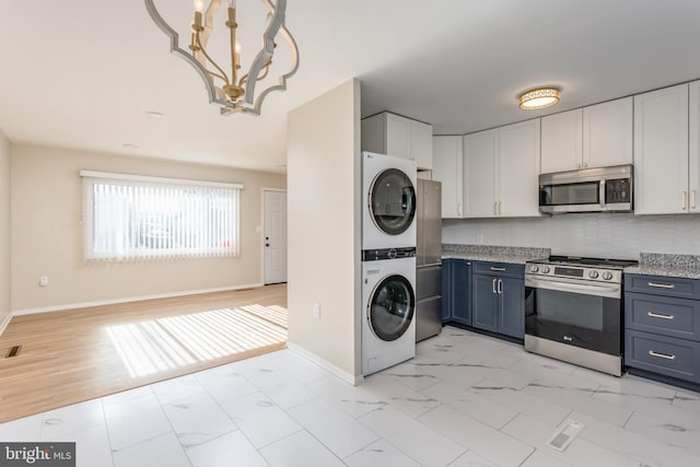 kitchen featuring blue cabinets, white cabinets, backsplash, stacked washer and dryer, and stainless steel appliances