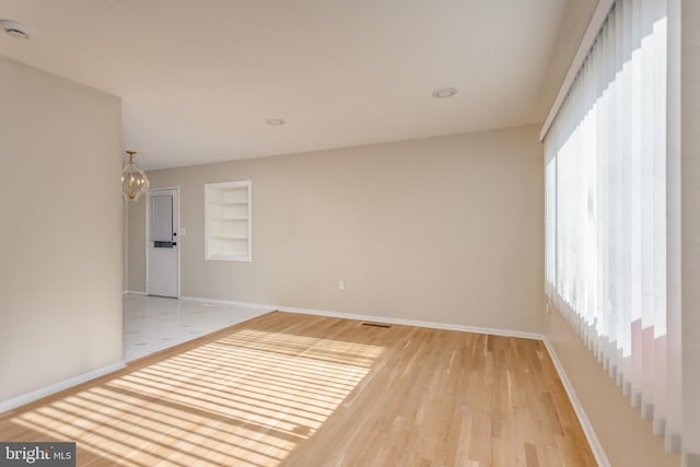 unfurnished room with an inviting chandelier, a wealth of natural light, built in features, and light wood-type flooring