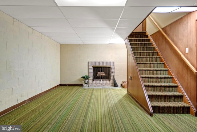 interior space featuring a fireplace, a paneled ceiling, wooden walls, and carpet