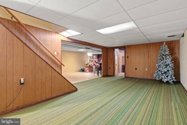 basement with carpet, a paneled ceiling, and wood walls