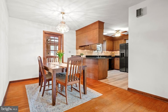 dining space with sink, ceiling fan with notable chandelier, and light hardwood / wood-style flooring