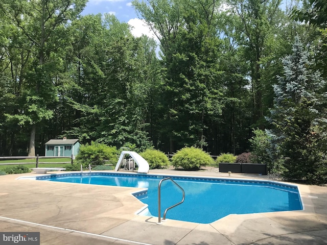 view of pool featuring a patio, a water slide, an outbuilding, and a diving board