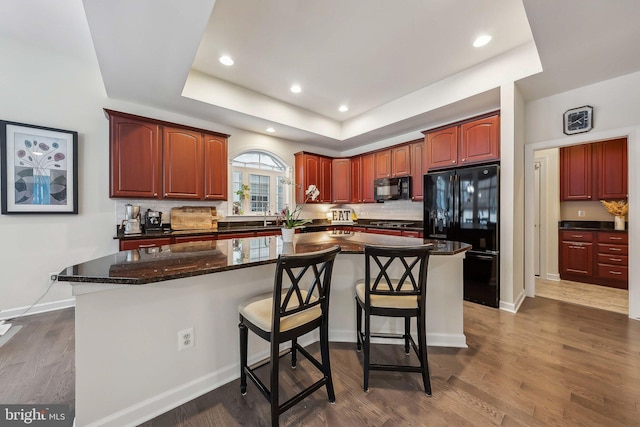 kitchen with a tray ceiling, a breakfast bar area, black appliances, and a kitchen island