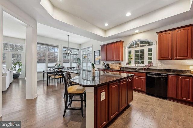 kitchen with decorative light fixtures, black dishwasher, sink, a center island, and light wood-type flooring