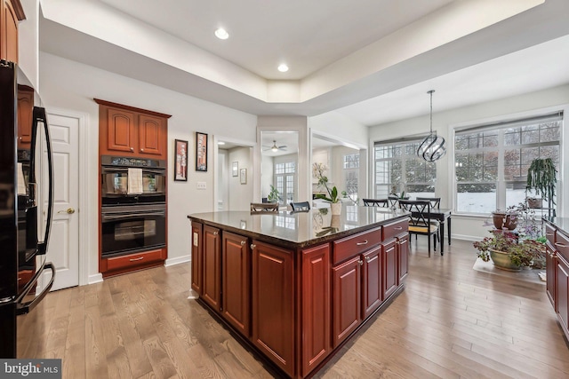 kitchen featuring hanging light fixtures, a center island, light hardwood / wood-style floors, black appliances, and a raised ceiling