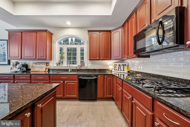 kitchen with sink, black appliances, decorative backsplash, dark stone counters, and light wood-type flooring