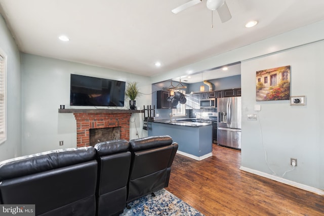 living room with a brick fireplace, dark wood-type flooring, sink, and ceiling fan