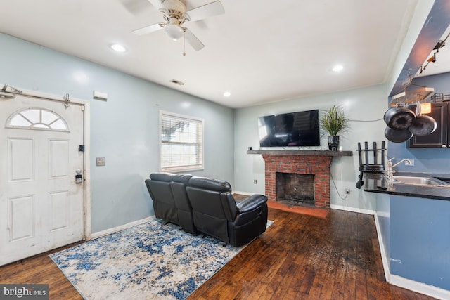 living room featuring dark wood-type flooring, ceiling fan, a fireplace, and sink