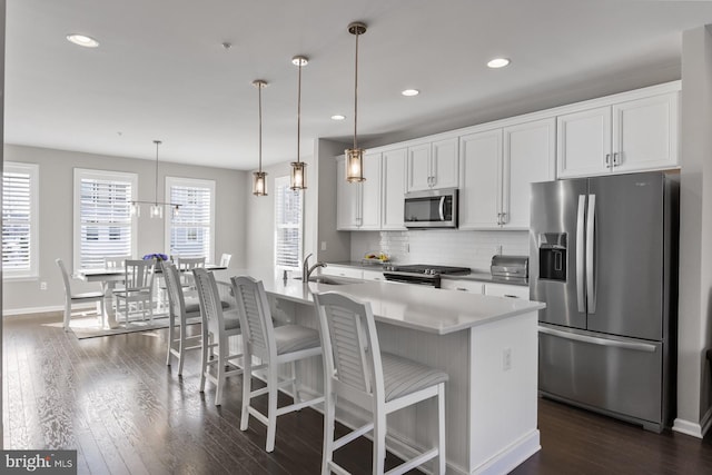 kitchen featuring pendant lighting, sink, white cabinets, stainless steel appliances, and a center island with sink