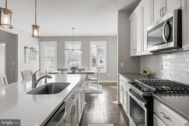 kitchen with sink, appliances with stainless steel finishes, white cabinets, dark hardwood / wood-style flooring, and decorative light fixtures