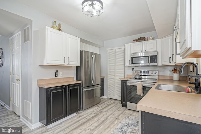 kitchen with sink, stainless steel appliances, white cabinets, and light wood-type flooring