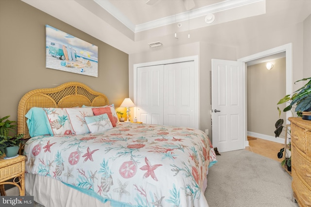 bedroom with crown molding, a closet, a tray ceiling, and light colored carpet