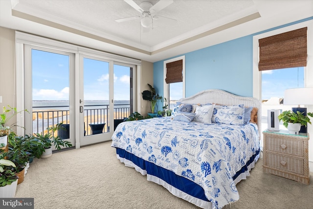 bedroom featuring a water view, carpet floors, access to outside, and a raised ceiling