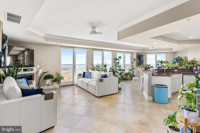 tiled living room with a fireplace, a textured ceiling, ceiling fan, and a raised ceiling