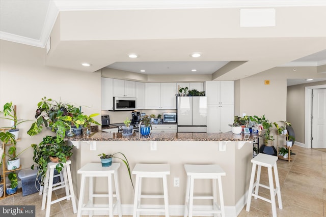 kitchen featuring a breakfast bar area, stone countertops, white appliances, white cabinetry, and kitchen peninsula