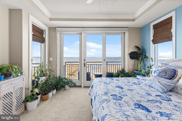 bedroom with carpet, access to outside, a water view, a tray ceiling, and ornamental molding