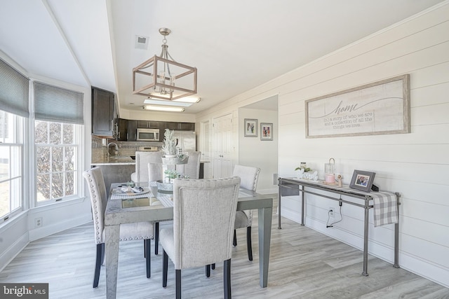 dining space with wooden walls, sink, and light hardwood / wood-style flooring