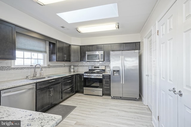 kitchen with stainless steel appliances, sink, light stone counters, and decorative backsplash