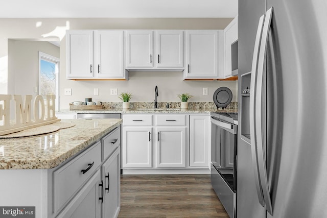 kitchen featuring stainless steel appliances, white cabinetry, light stone countertops, and dark wood-type flooring