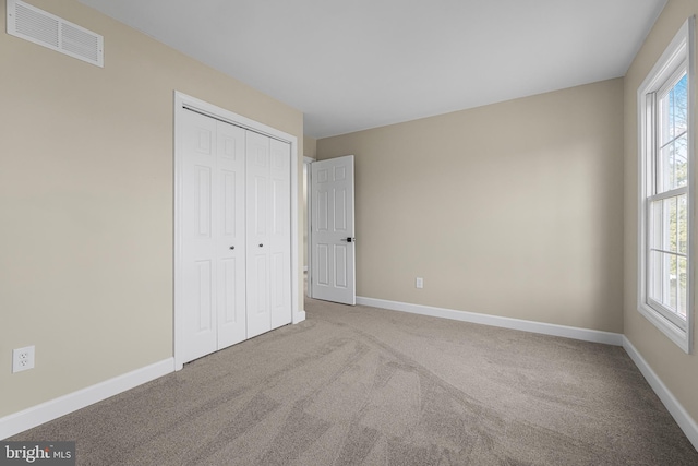 unfurnished bedroom with multiple windows, light colored carpet, and a closet