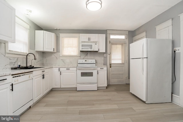 kitchen with white cabinetry, sink, backsplash, light stone countertops, and white appliances