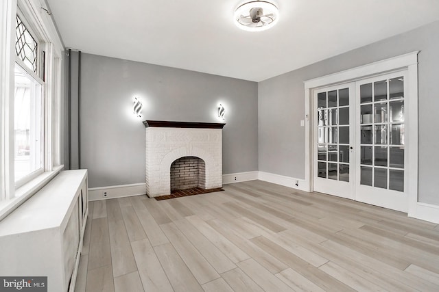 unfurnished living room with a brick fireplace, light wood-type flooring, and french doors