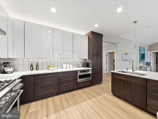 kitchen with sink, white cabinetry, hanging light fixtures, light wood-type flooring, and stainless steel appliances