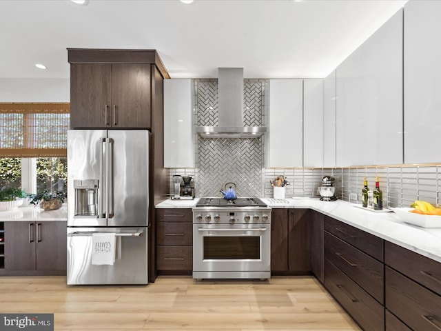 kitchen featuring tasteful backsplash, premium appliances, white cabinets, wall chimney exhaust hood, and light wood-type flooring