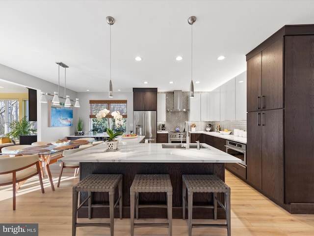 kitchen with pendant lighting, white cabinetry, a kitchen island with sink, stainless steel appliances, and wall chimney exhaust hood