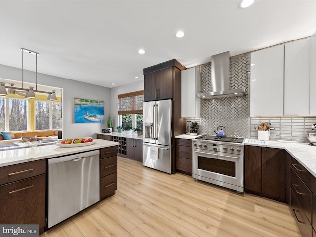 kitchen with white cabinetry, high end appliances, wall chimney range hood, and decorative backsplash