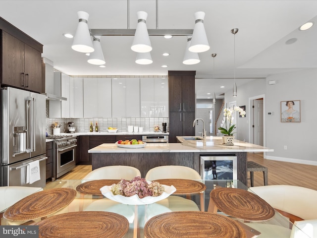 kitchen featuring decorative light fixtures, high quality appliances, an island with sink, white cabinets, and dark brown cabinets