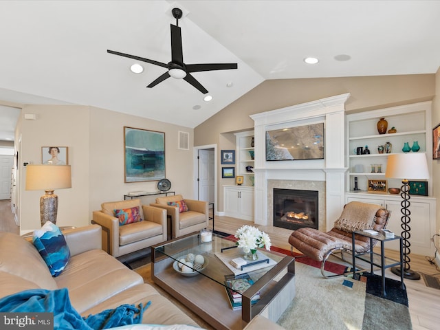 living room featuring lofted ceiling, built in shelves, light hardwood / wood-style flooring, and ceiling fan