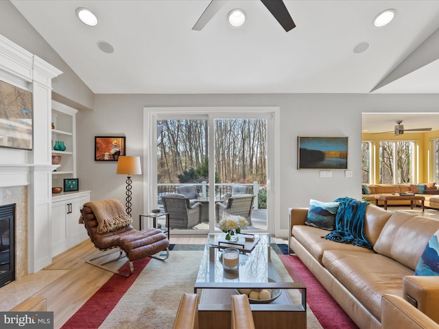 living room featuring vaulted ceiling, built in features, a tiled fireplace, ceiling fan, and light wood-type flooring