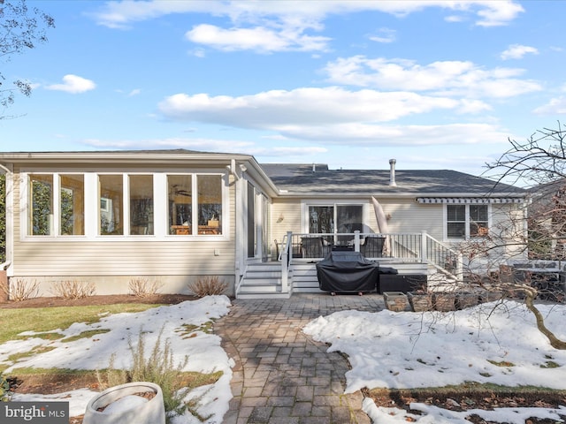 snow covered back of property with a wooden deck and a patio