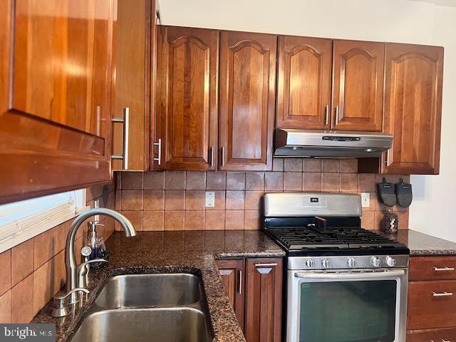 kitchen with gas range, dark stone counters, sink, and backsplash