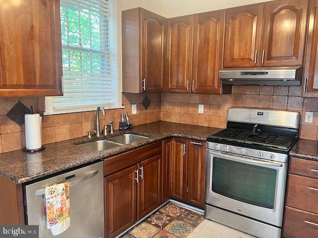 kitchen with backsplash, stainless steel appliances, sink, and dark stone countertops