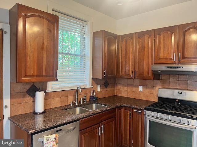 kitchen featuring sink, decorative backsplash, stainless steel appliances, and dark stone counters