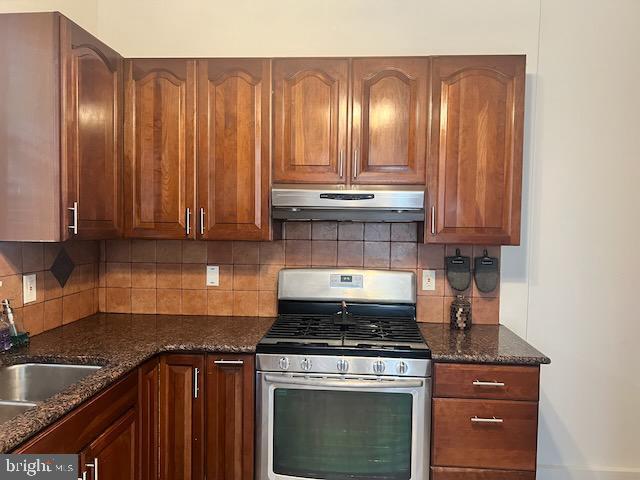 kitchen with gas stove, sink, dark stone countertops, and decorative backsplash