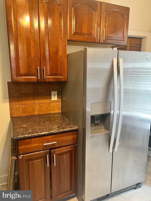 kitchen featuring dark stone countertops, stainless steel fridge with ice dispenser, and decorative backsplash