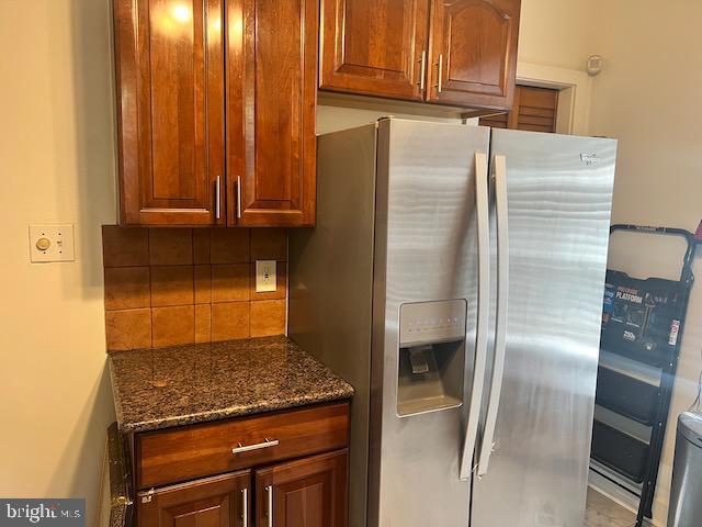 kitchen with stainless steel fridge, decorative backsplash, and dark stone countertops